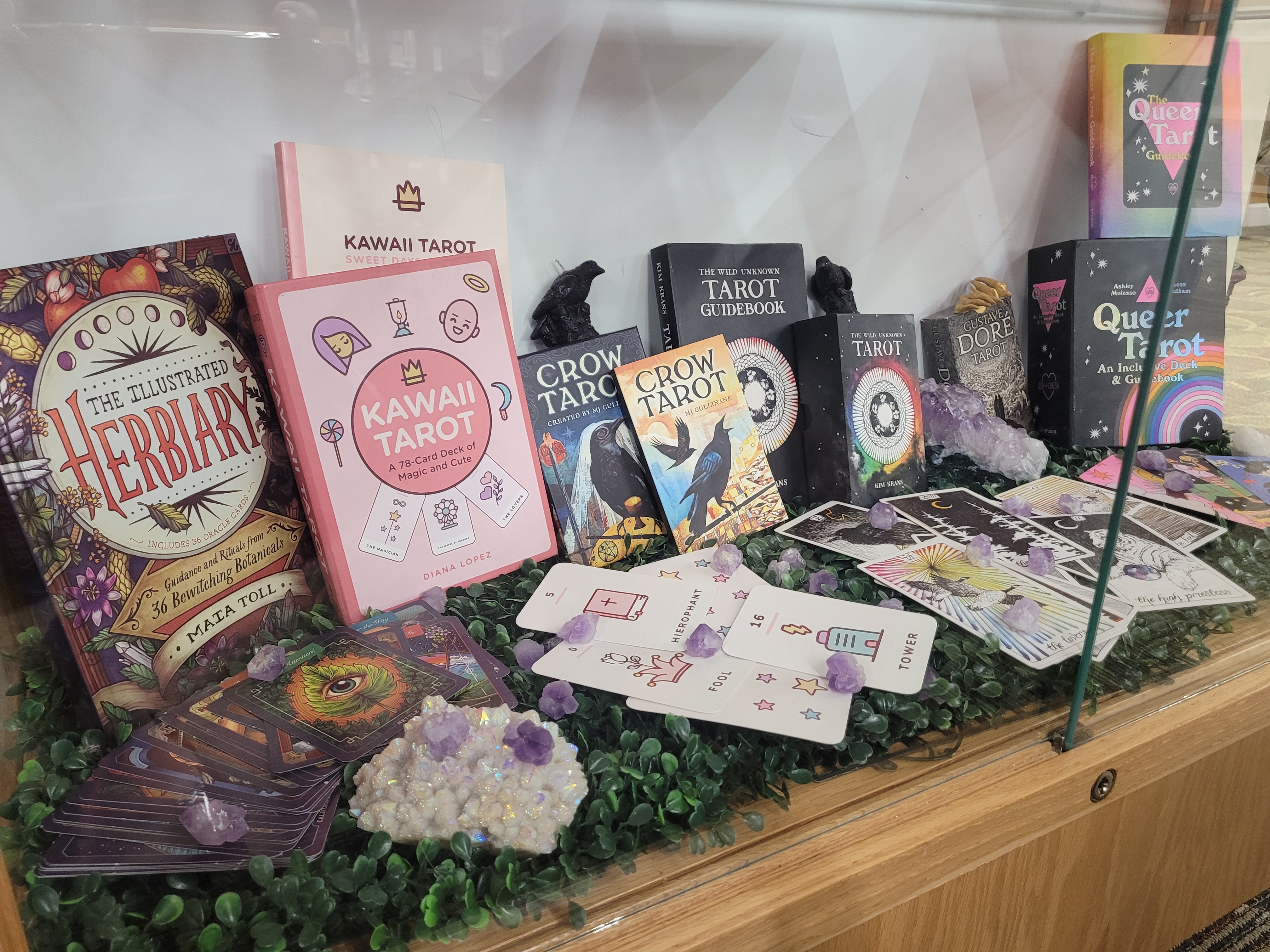 Several tarot decks in a little display case on top of fake wild grass and real crystals scattered around the guidebooks, cases, and spread-out decks.