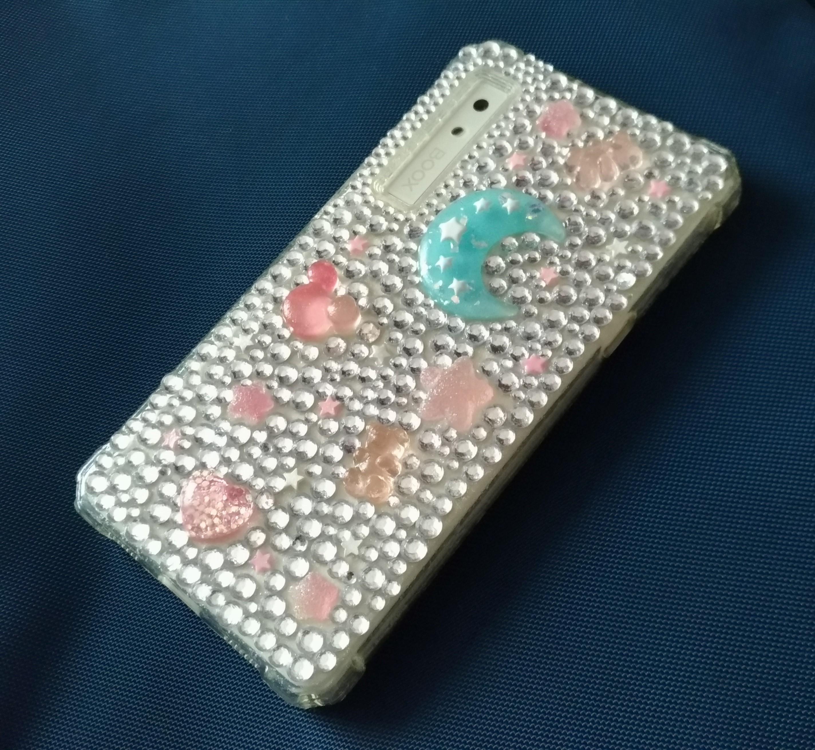 Bedazzled phone case with a soft blue moon resin charm, as well as some pink star and gummy bear charms. There's one cute pink mickey mouse symbol charm too.
